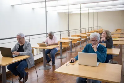 Elderly people enthusiastically using laptops in a classroom environment, embracing modern technology.