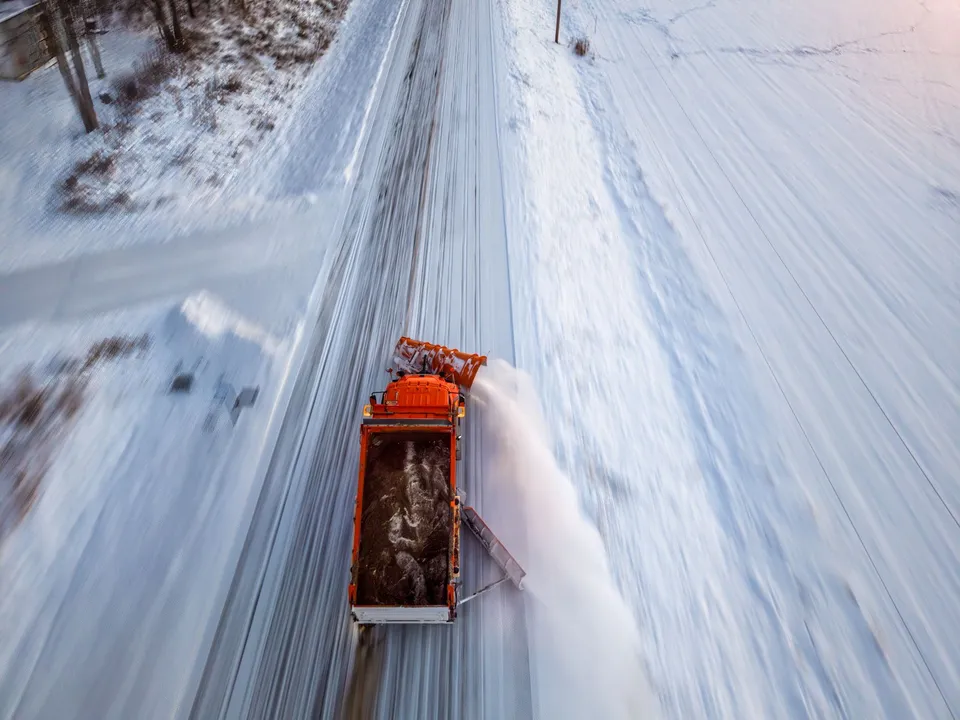 An orange snowplow clears a snow-covered road in Kellogg, Minnesota during winter.