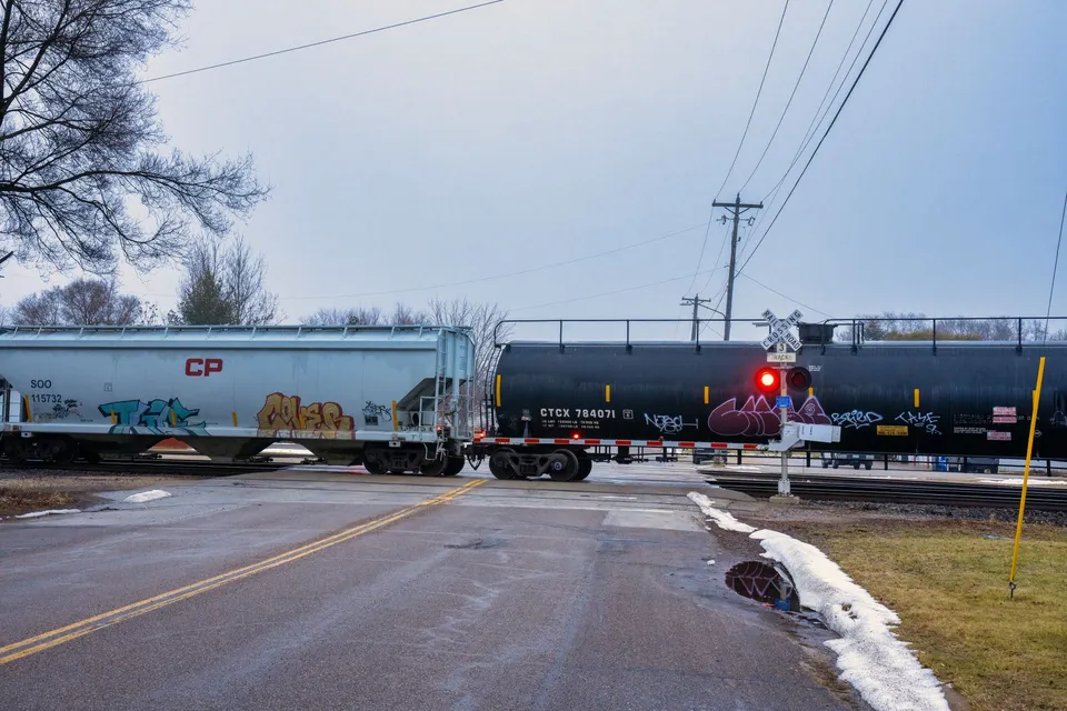 Freight train crossing a rural road in Wabasha, Minnesota during winter with visible graffiti.