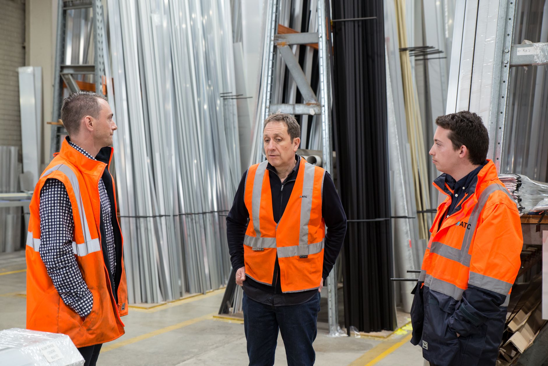 Team in high-visibility vests conversing in a metal warehouse.