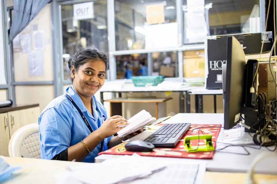 A cheerful female worker seated at her desk in an office setting, reviewing documents.