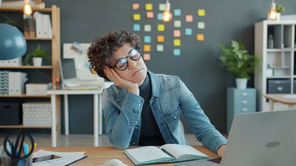 Woman falling asleep at her desk in an office, emphasizing workplace fatigue.